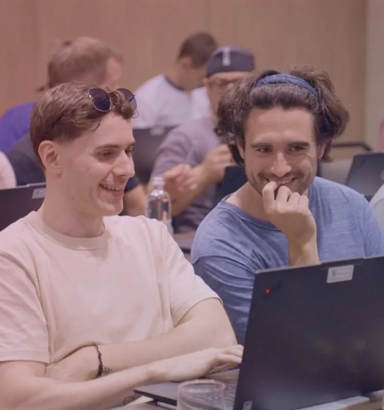 Colleghi che sorridono mentre lavorano ai laptop, seduti in fila