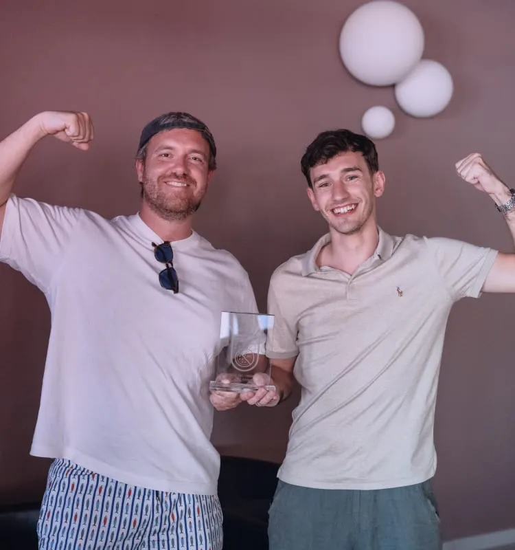 Due colleghi che mostrano i muscoli sorridendo, con un trofeo in mano
